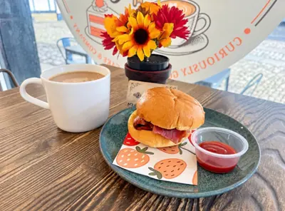 A bacon bap with ketchup and a hot drink