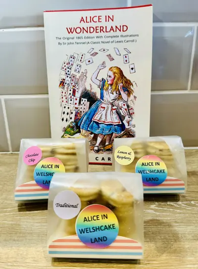Packs of Alice in Welshcake Land Welsh cakes in front of an Alice in Wonderland book